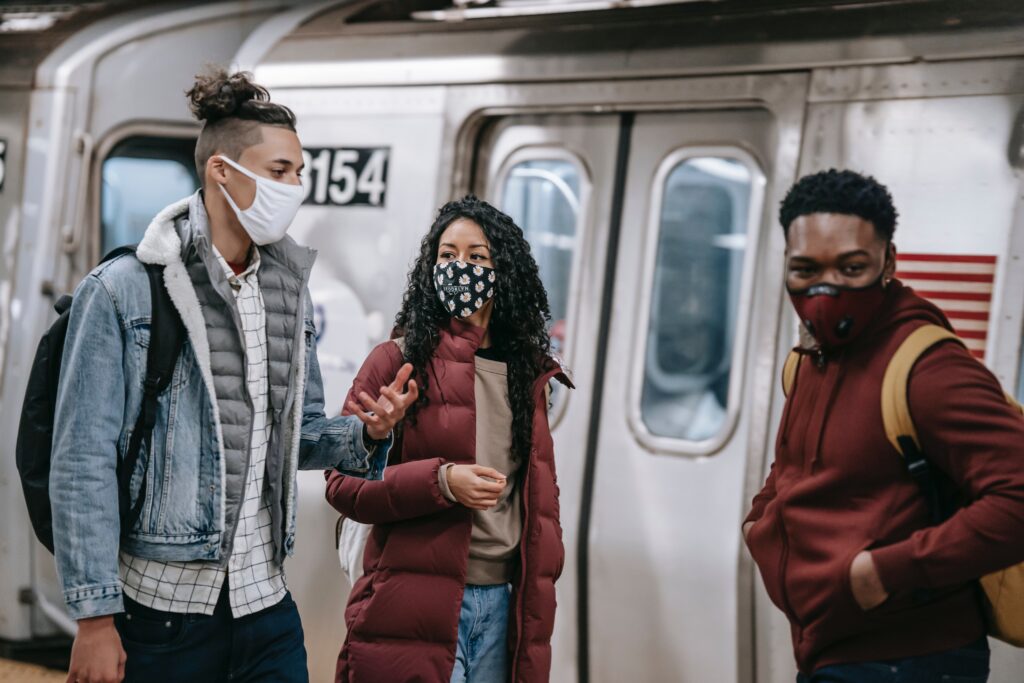 Young people wearing germ masks standing in front of train doors
